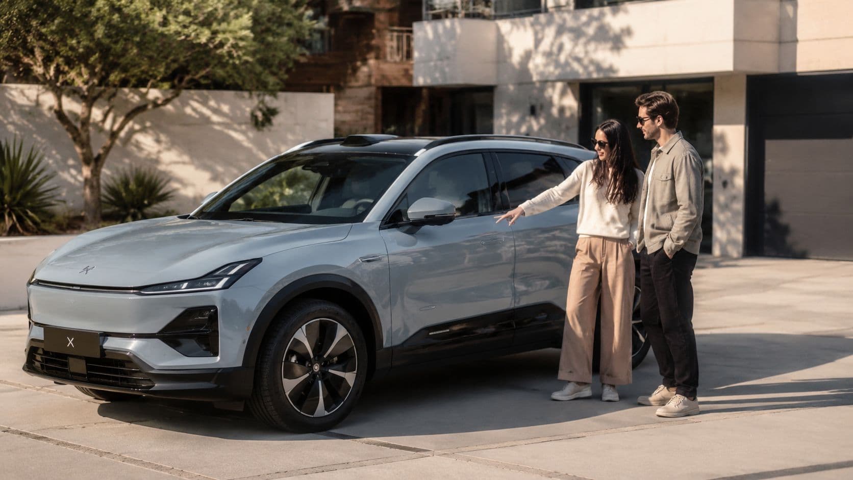 Una pareja joven observa y señala su nuevo coche eléctrico tipo SUV aparcado frente a una casa moderna.